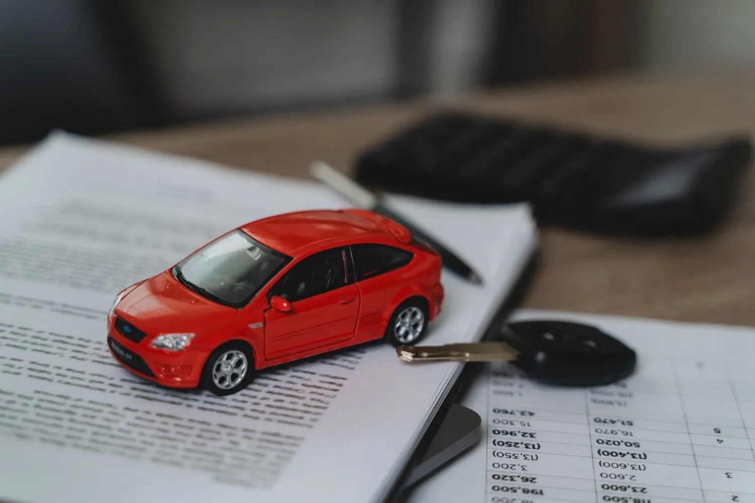 Small red model car and a set of keys resting on a policy document